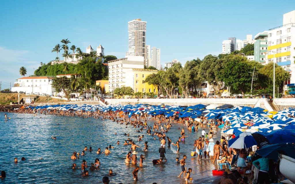 Praia movimentada em Salvador, com guarda-sóis coloridos e pessoas aproveitando o dia ensolarado.