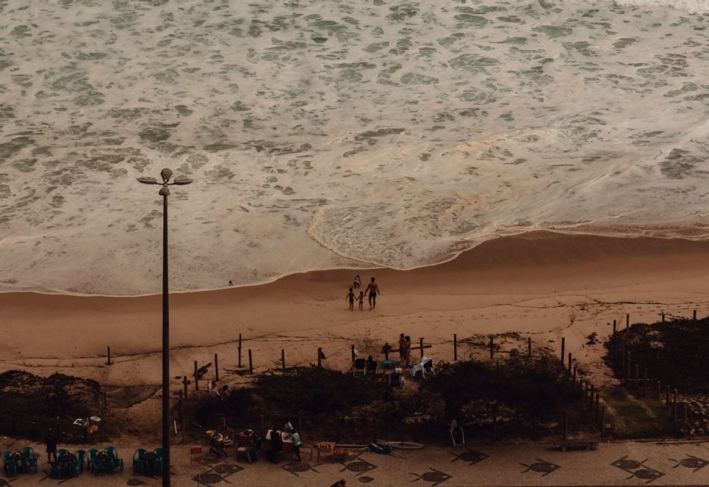 Levantamento do Turismo buscará entender visitantes em 50 destinos do país Vista aérea de famílias aproveitando a praia no Rio de Janeiro.