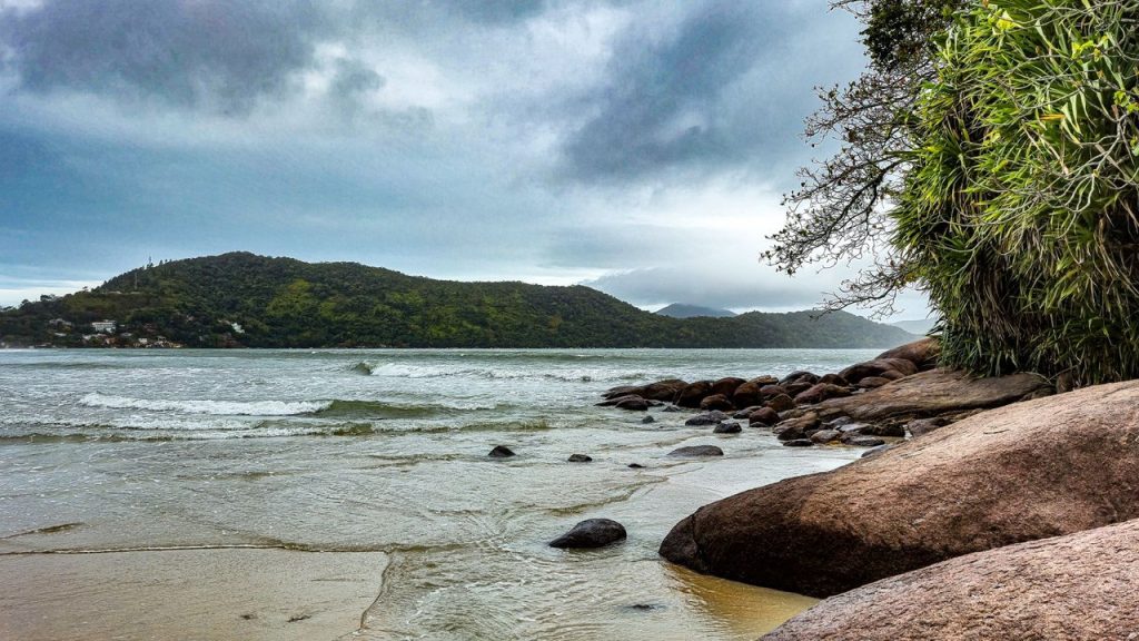 Praia da Enseada, em Ubatuba, com mar calmo, faixa de areia e morros cobertos por vegetação.