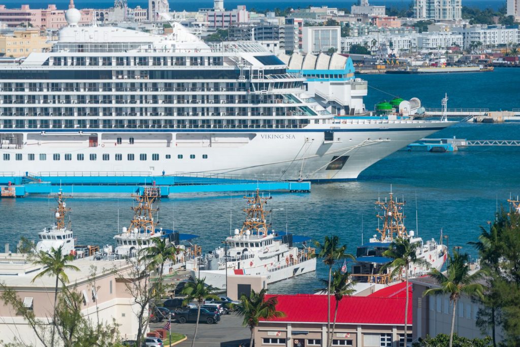 Navio de cruzeiro atracado em uma marina urbana, com edifícios ao fundo.