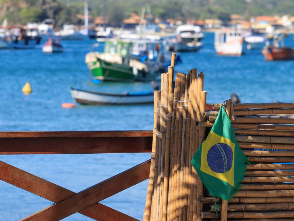 Bandeira do Brasil diante de barcos ancorados em uma baía costeira.